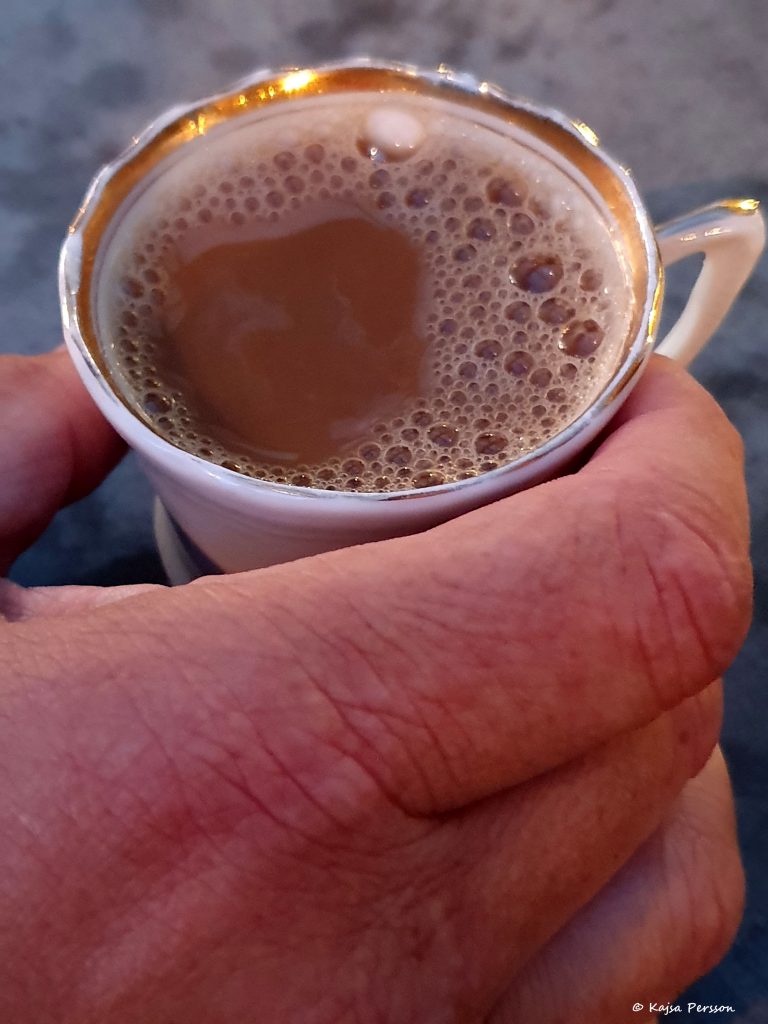 En hand med en liten porslinskopp med kaffe