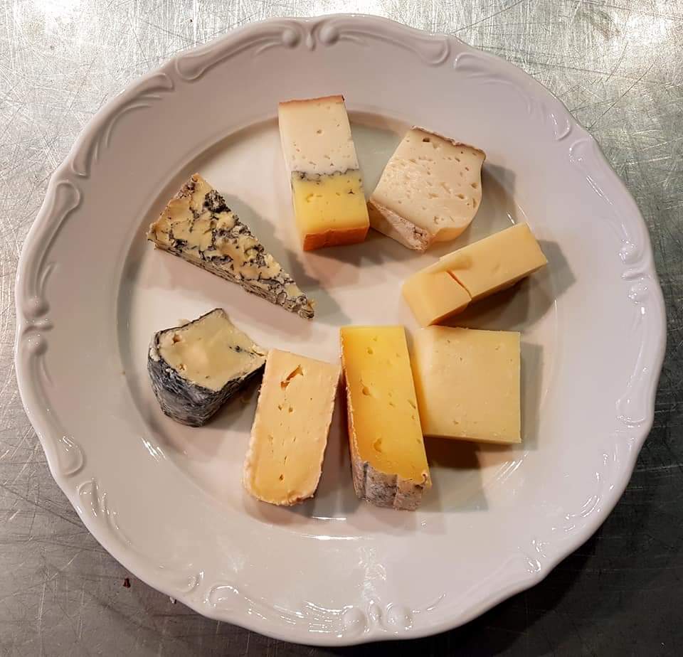Vit tallrik med 8 bitar ost av olika slag till ostprovning.