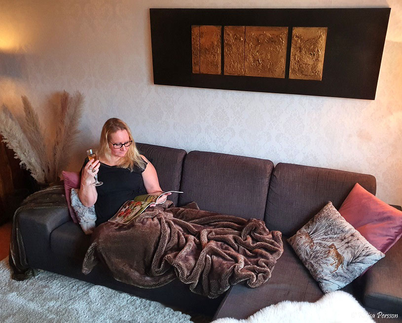 Kvinna i soffan som läser tidning och dricker champagne