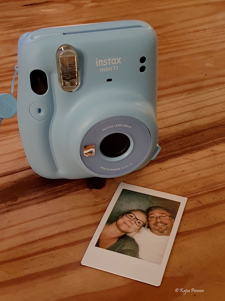 Ljusblå polaroidkamera med ett foto på ett bord