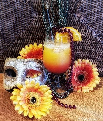 Fruktig gul och orange drink, pärlor i rött och grönt, blommor och en maskeradmask